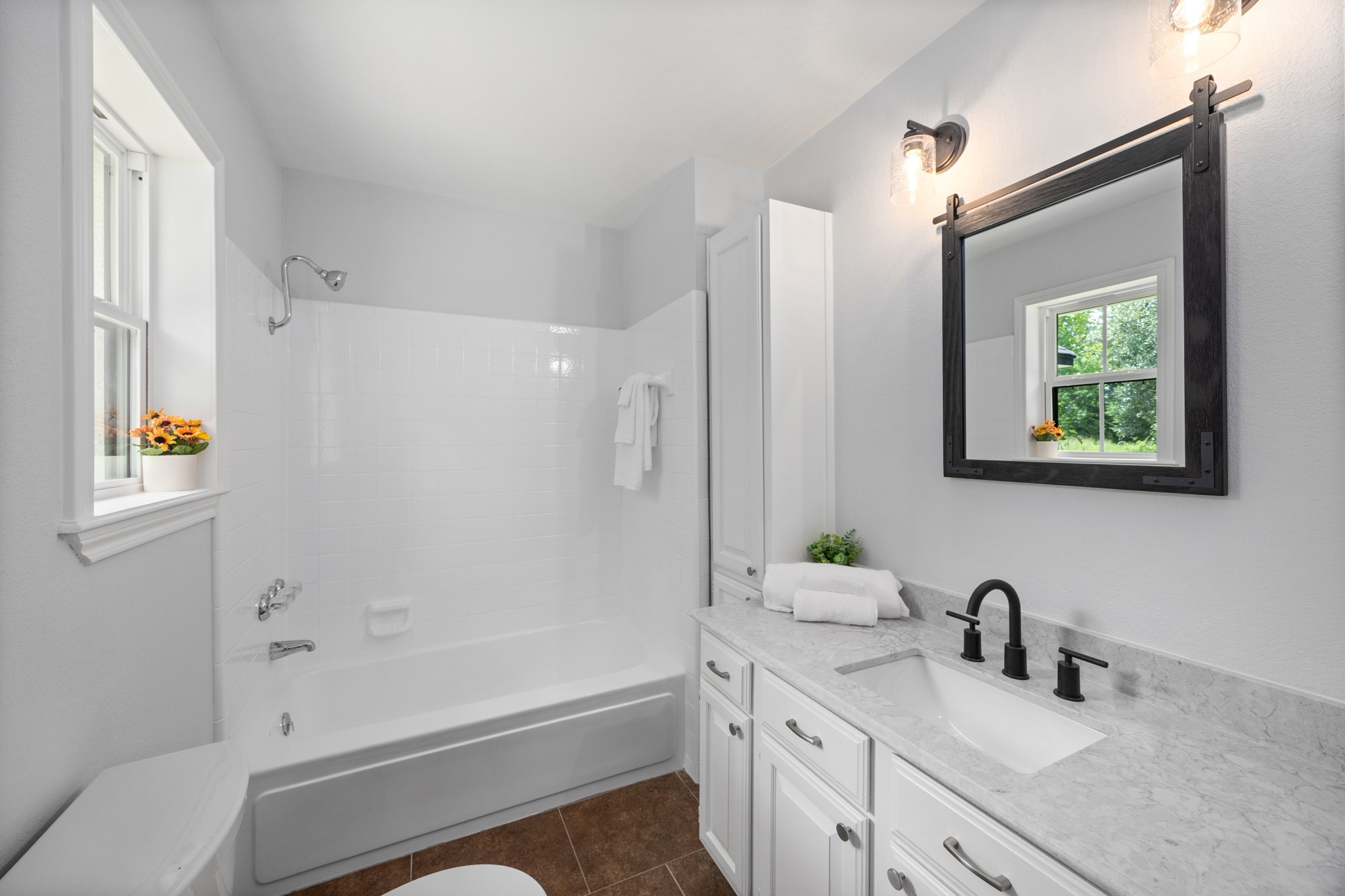 10209 Oberrender Road Needville, TX 77461 - Photo 30 of 50 Bright, modern primary bathroom featuring a clean white design, granite countertop, and stylish black fixtures. Includes a bathtub with shower, a window for natural light, and ample storage space.