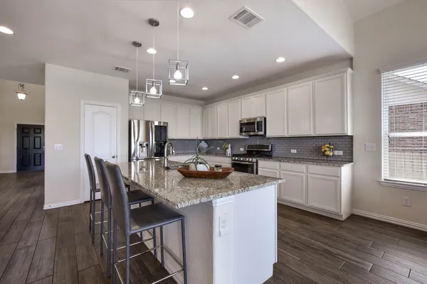 a kitchen with stainless steel appliances granite countertop a stove top oven a refrigerator a sink and a dining table with wooden floor