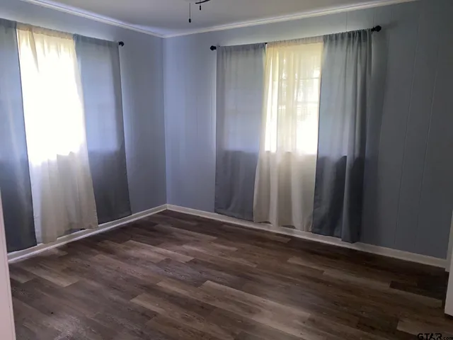an empty room with wooden floor and windows with curtains