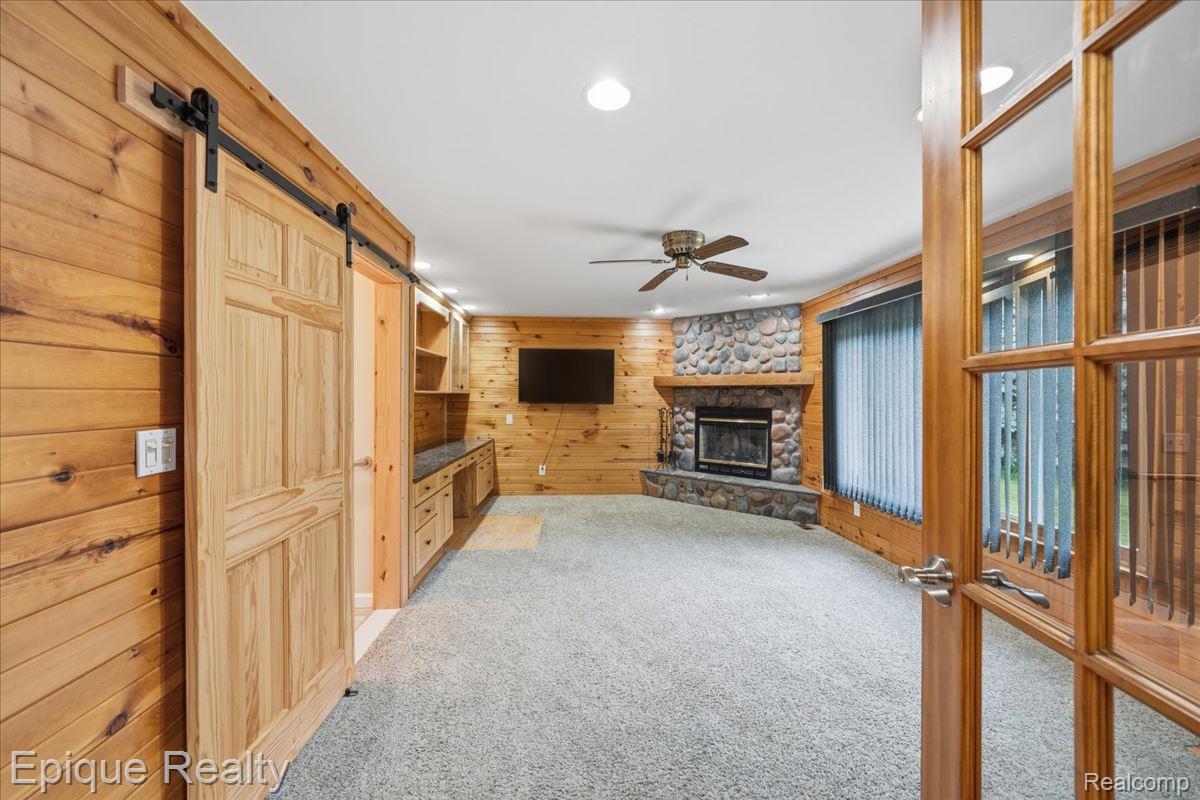 1221 Rhodes Road Lake Orion, MI 48360 - Photo 27 of 72 Spacious room featuring wood paneling, a stone-faced fireplace, and light-toned carpeting