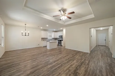 a view of an empty room and kitchen with wooden floor