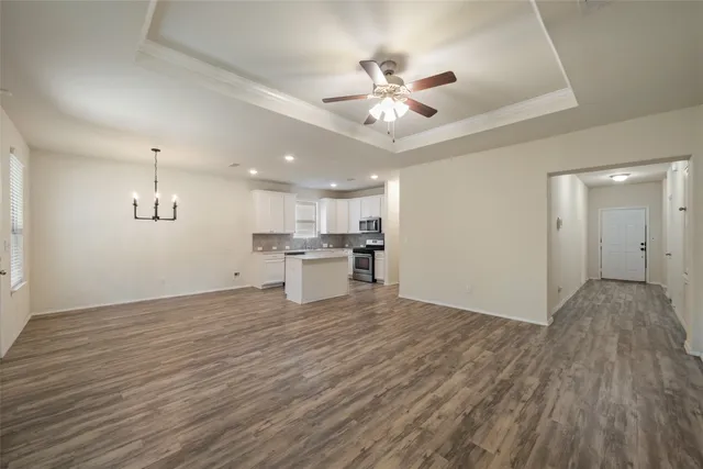a view of an empty room and kitchen with wooden floor