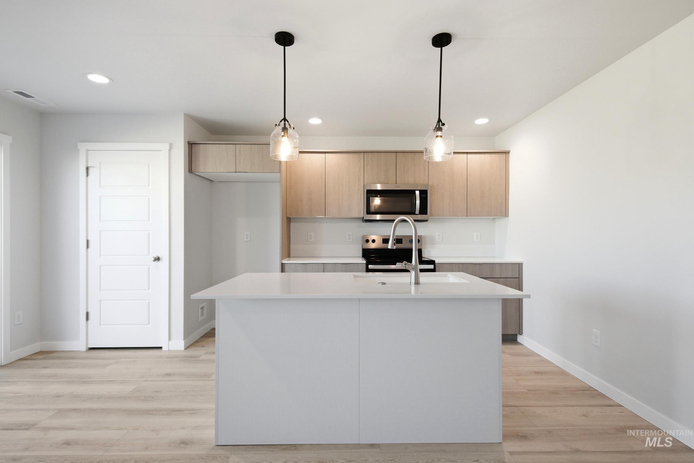 10800 Rutland Street Caldwell, ID 83605 - Photo 2 of 21 Open-concept kitchen featuring an island with a built-in sink and pendant lighting, light wood-finish cabinetry, stainless steel appliances, and wood-finish flooring
