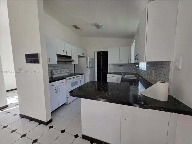a kitchen with granite countertop white cabinets a refrigerator and a sink