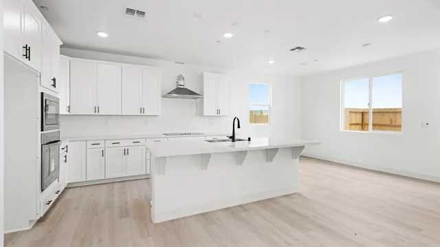 a large kitchen with stainless steel appliances granite countertop a stove a sink a refrigerator and white cabinets with wooden floor