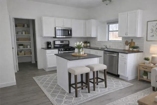 a kitchen with stainless steel appliances granite countertop a stove top oven a sink dishwasher and a dining table with wooden floor