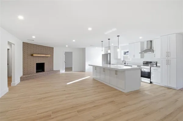 a large kitchen with kitchen island a sink dishwasher a refrigerator and white cabinets with wooden floor