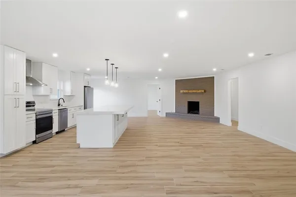 a large kitchen with kitchen island a stove a sink dishwasher a refrigerator and white cabinets with wooden floor