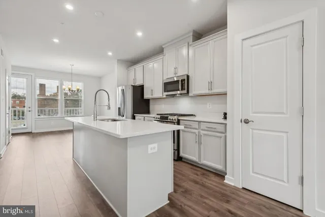 a kitchen with stainless steel appliances granite countertop a stove top oven a sink a refrigerator and white cabinets with wooden floor