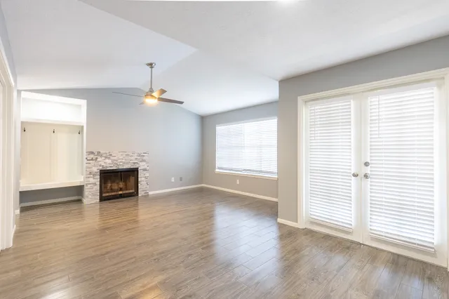 an empty room with wooden floor fireplace and windows