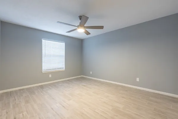 an empty room with wooden floor ceiling fan and windows