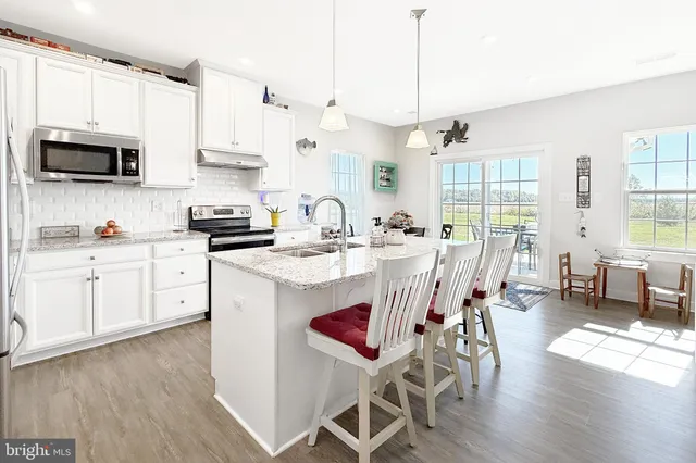 a kitchen with stainless steel appliances granite countertop a stove a sink a microwave a dining table and chairs with wooden floor