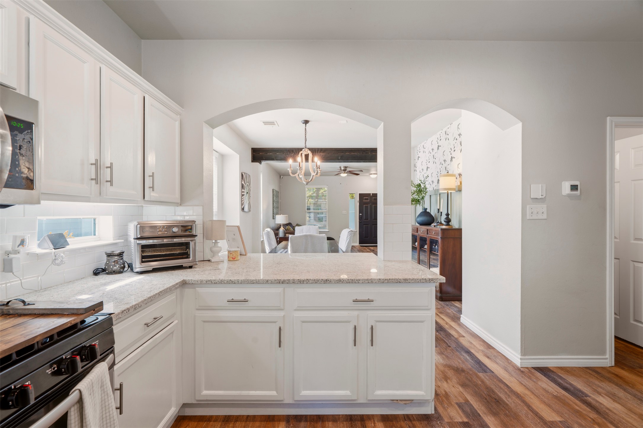913 Bogart Road Cedar Park, TX 78613 - Photo 7 of 27 Kitchen featuring a peninsula, white cabinetry, tasteful backsplash, arched walkways, and light stone countertops