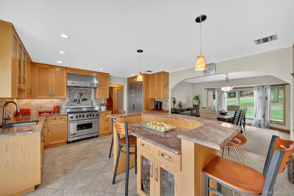 a dining hall with stainless steel appliances kitchen island granite countertop a dining table chairs and a refrigerator