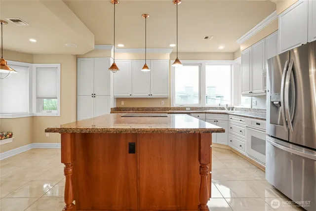 a kitchen with stainless steel appliances granite countertop a refrigerator a sink dishwasher a stove and white cabinets with wooden floor