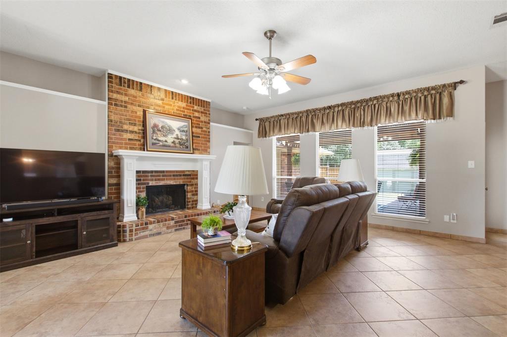 4218 Glistening Spring Rowlett, TX 75088 - Photo 7 of 39 Living area featuring a brick fireplace with a white mantel, ceiling fan with light fixture, large windows, and tile flooring