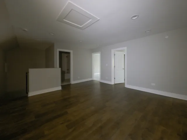 a view of an empty room with wooden floor and a ceiling fan