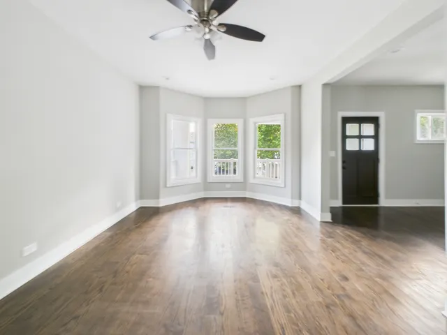 an empty room with wooden floor fan and windows