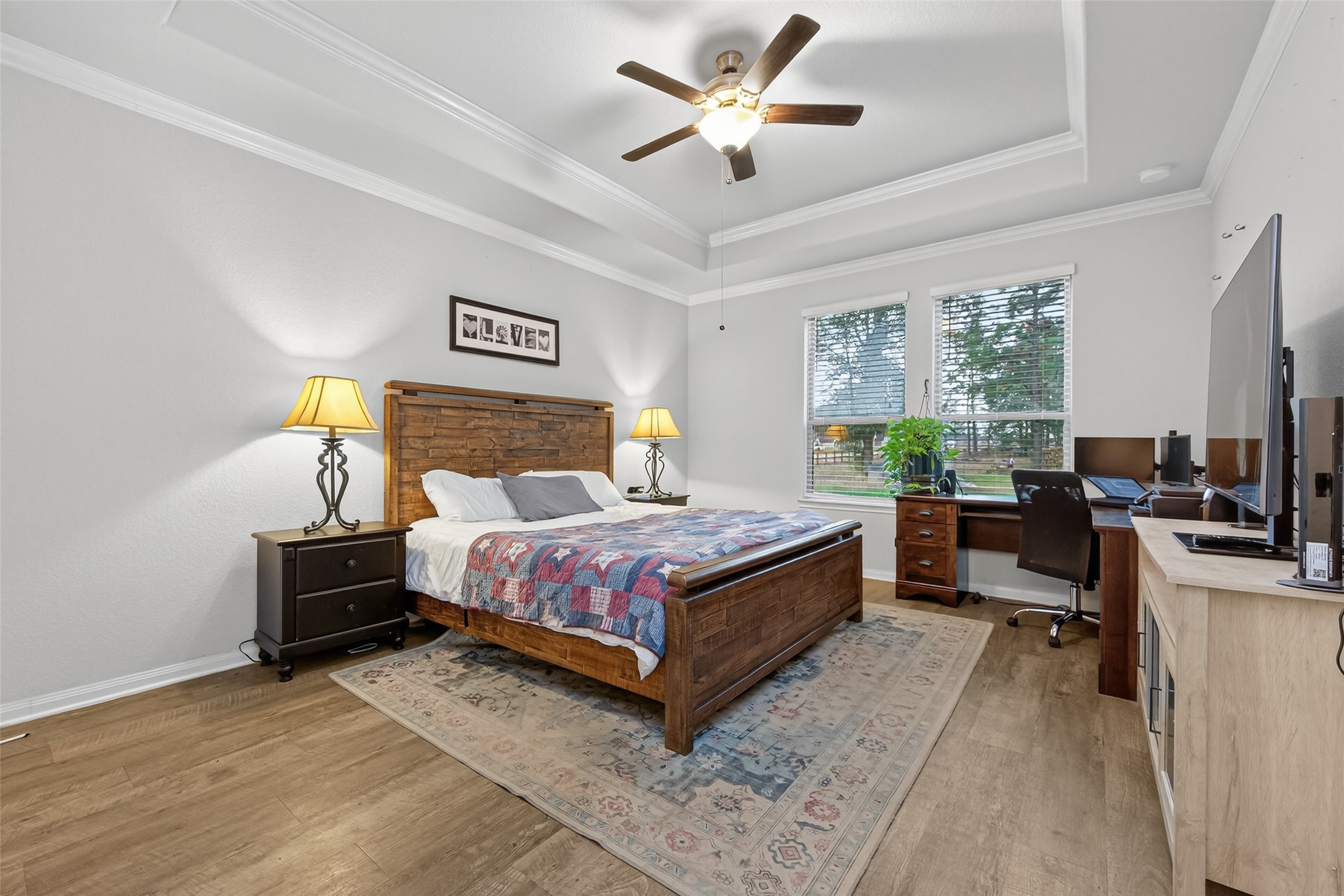 16601 Crosby Street Conroe, TX 77303 - Photo 22 of 50 Spacious primary bedroom featuring a tray ceiling, wood-look flooring, and large windows that bring in beautiful natural light.
