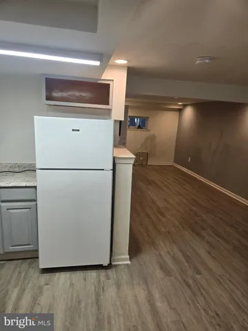 a view of a refrigerator in kitchen and an empty room with wooden floor