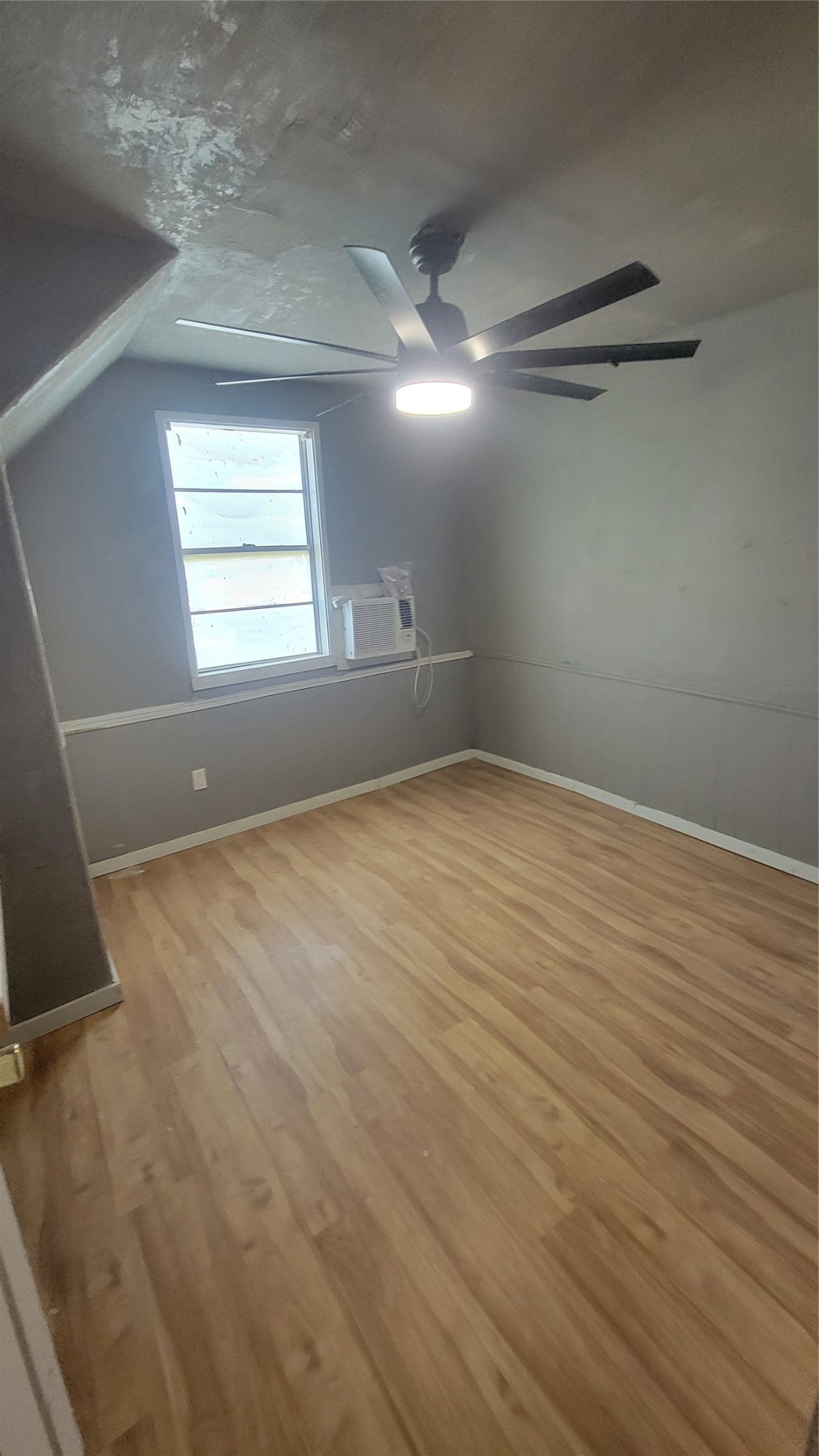 12018 Sandpiper Road Angleton, TX 77515 - Photo 22 of 48 This room features laminate wood flooring, a ceiling fan with light, and a window with an air conditioning unit. It has neutral gray walls and a sloped ceiling, providing a cozy atmosphere.