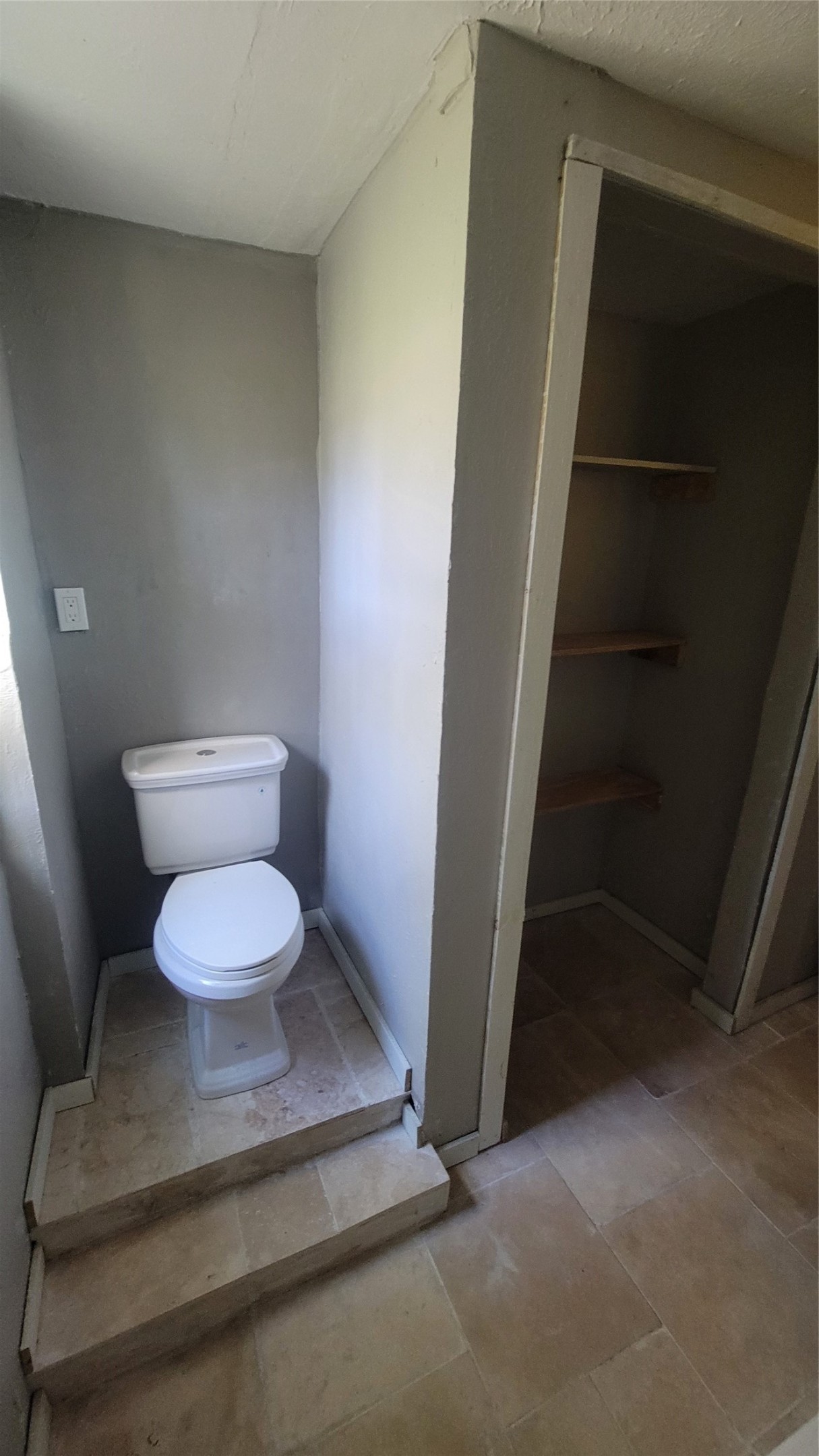 12018 Sandpiper Road Angleton, TX 77515 - Photo 27 of 48 This photo shows a compact bathroom area with a raised toilet platform and adjacent shelving space, featuring neutral-colored tiled flooring and walls.