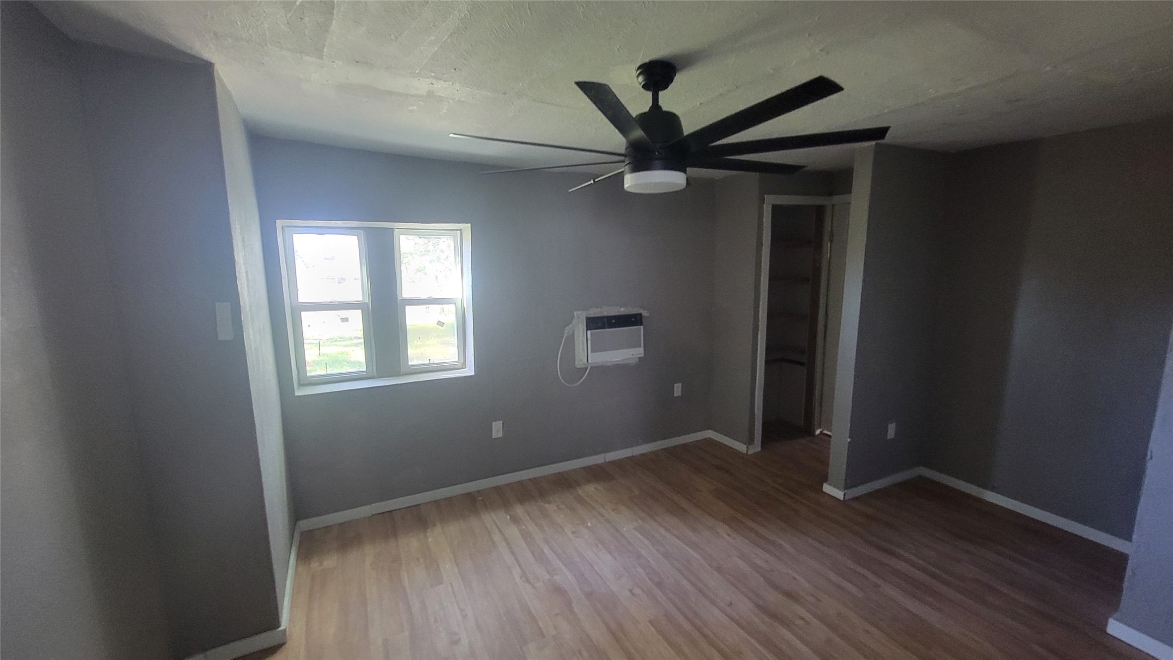 12018 Sandpiper Road Angleton, TX 77515 - Photo 29 of 48 A cozy room with light wood flooring and neutral gray walls, featuring a ceiling fan and a window for natural light. There's a wall-mounted air conditioner and a small closet space for storage.