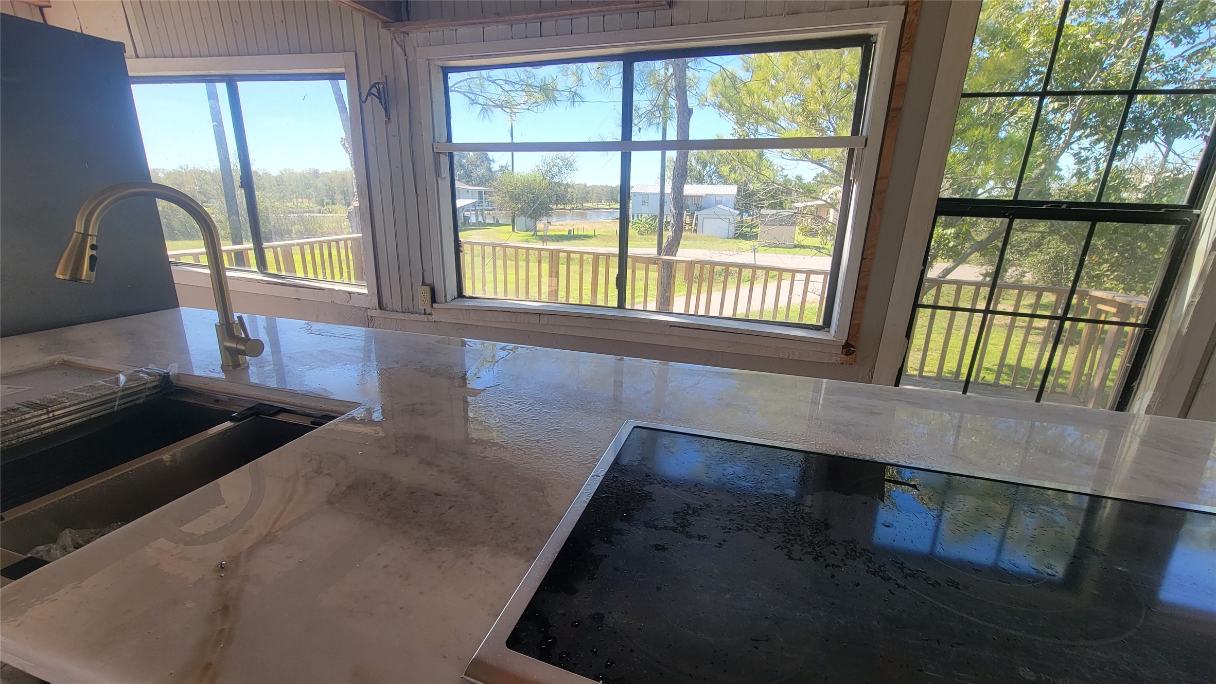 12018 Sandpiper Road Angleton, TX 77515 - Photo 10 of 48 This photo showcases a modern kitchen with a large, glossy countertop and a built-in sink. The space is bright, featuring expansive windows with views of a green, tree-lined area and a nearby street, creating a welcoming atmosphere.