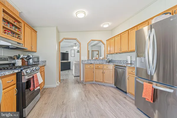 a kitchen with stainless steel appliances granite countertop a refrigerator a sink dishwasher a stove and white countertops with wooden floor