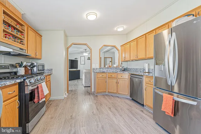 a kitchen with stainless steel appliances granite countertop a refrigerator a sink dishwasher a stove and white countertops with wooden floor