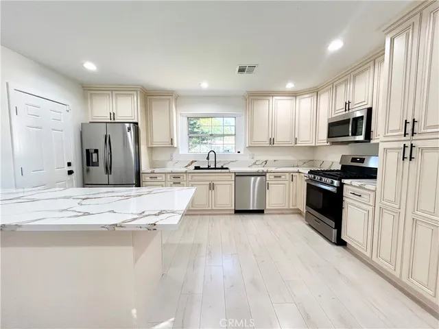 a kitchen with stainless steel appliances kitchen island granite countertop a stove a sink a refrigerator and white cabinets