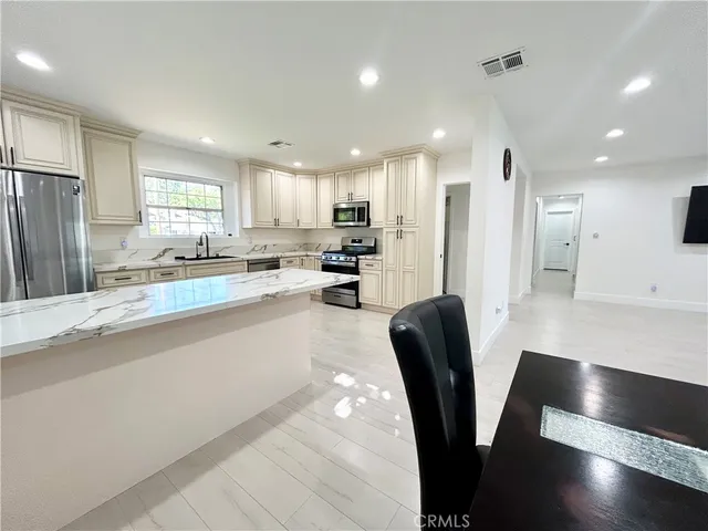 a kitchen with stainless steel appliances granite countertop a refrigerator a sink a stove a dining table and chairs