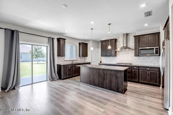 a large kitchen with stainless steel appliances granite countertop a stove a sink dishwasher a refrigerator and a microwave oven with wooden floor