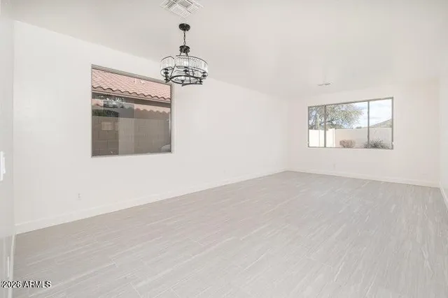 an empty room with wooden floor chandelier and windows