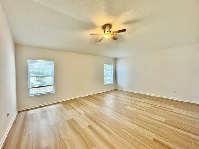a view of empty room with wooden floor and fan