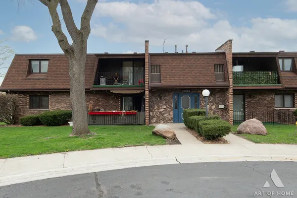 a view of a brick house with a yard plants and a large tree
