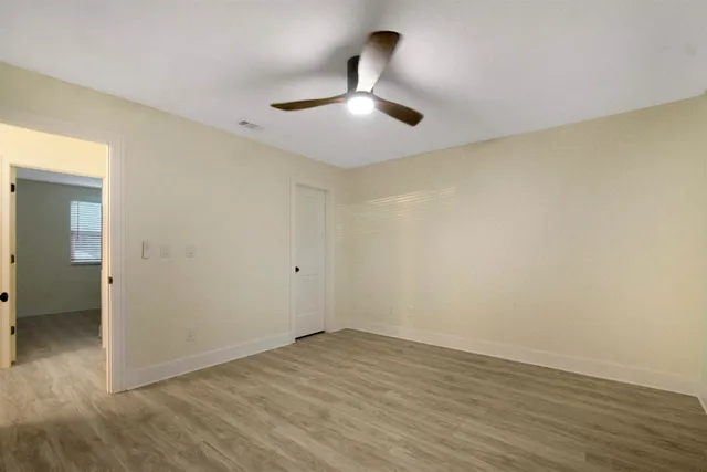 an empty room with wooden floor and fan