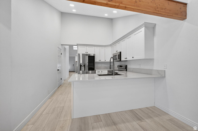 6969 South 855 East Midvale, UT 84047 - Photo 19 of 55 Modern kitchen with white cabinetry and light-toned countertops, featuring stainless steel appliances, a bar-height counter, and wood-finish flooring