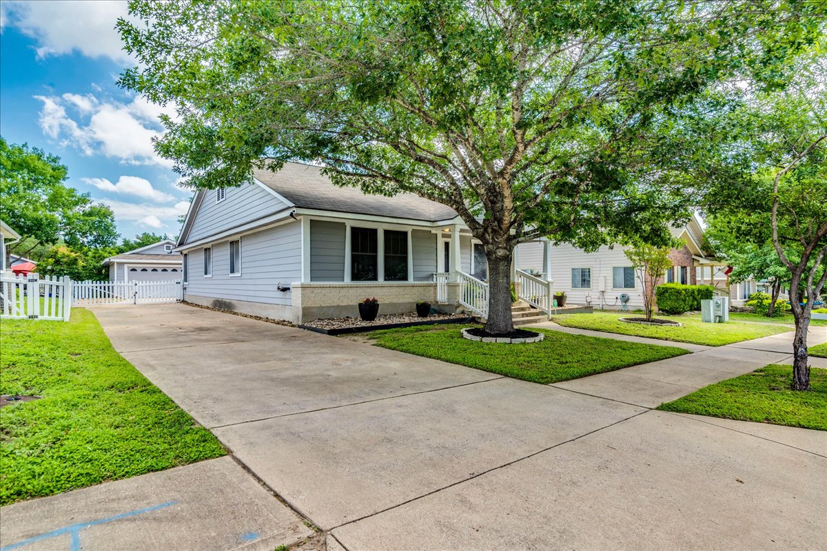 175 Wetzel Kyle, TX 78640 - Photo 7 of 27 Mature trees frame a charming home with a concrete driveway and picket fence.
