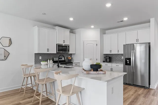 a kitchen with stainless steel appliances kitchen island granite countertop a refrigerator a stove a sink a dining table and chairs with wooden floor