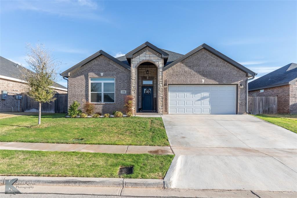 View of front of house with concrete driveway, fence, an attached garage, brick siding, and a front lawn
