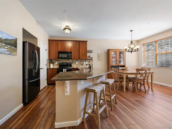 a kitchen with stainless steel appliances granite countertop a refrigerator a stove a microwave oven a dining table and chairs with wooden floor