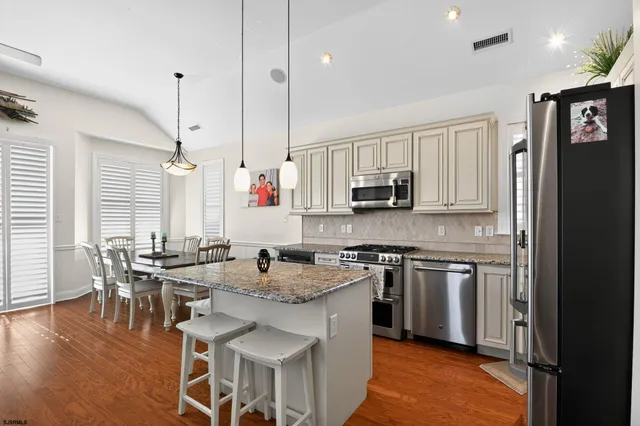 a kitchen with stainless steel appliances granite countertop a stove top oven a sink a dining table and chairs with wooden floor