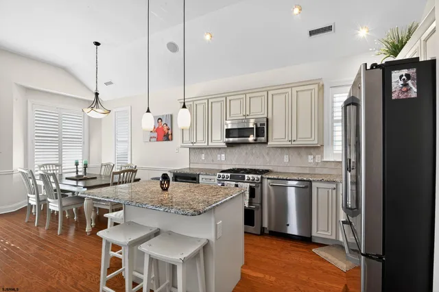 a kitchen with stainless steel appliances granite countertop a stove top oven a refrigerator a sink and a dining table with wooden floor