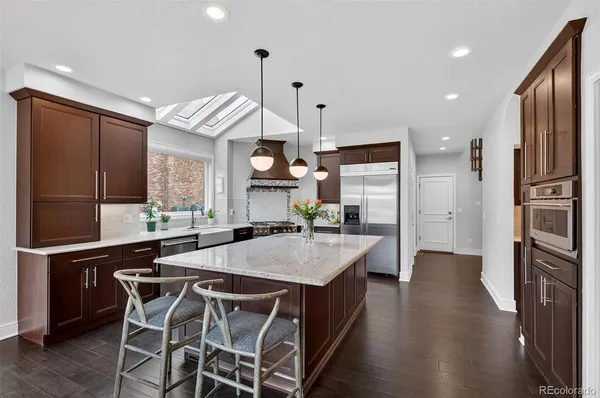 a kitchen with stainless steel appliances kitchen island granite countertop a refrigerator a stove and a sink with wooden floor