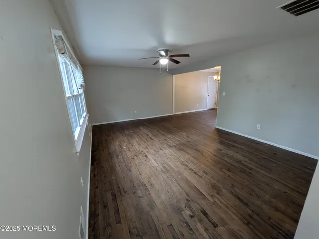 an empty room with wooden floor chandelier fan and windows