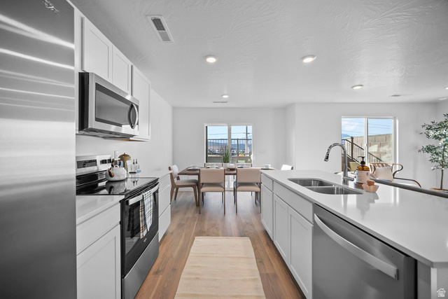 2123 Wolverine Way, Unit 2437 Washington, UT 84780 - Photo 18 of 40 Open-concept kitchen featuring stainless steel appliances, light wood-finish flooring, white cabinetry, a kitchen island with an undermount sink, and recessed lighting