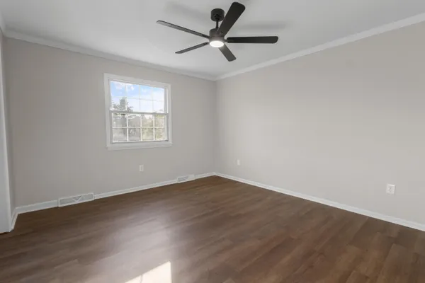 an empty room with wooden floor fan and windows