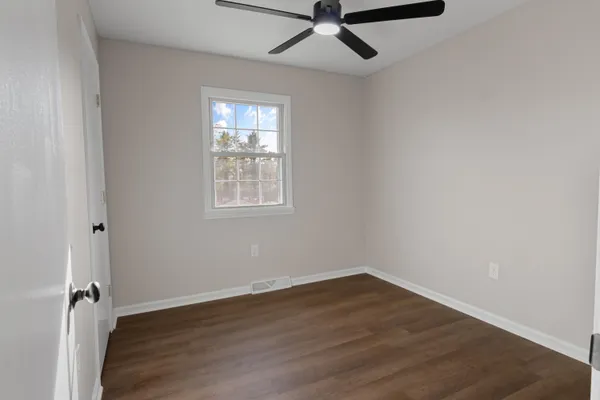 an empty room with wooden floor fan and windows