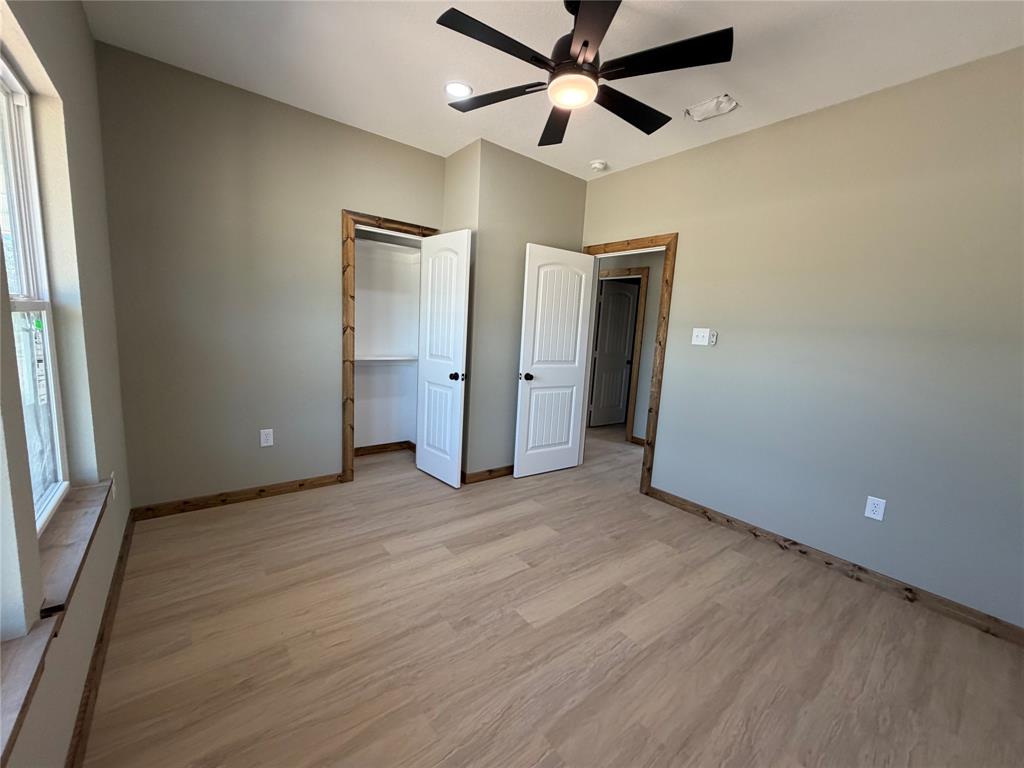 1040 Rays Way Weatherford, TX 76085 - Photo 17 of 23 Spacious bedroom featuring wood-finish flooring, a ceiling fan with integrated lighting, and multiple doors with wood trim